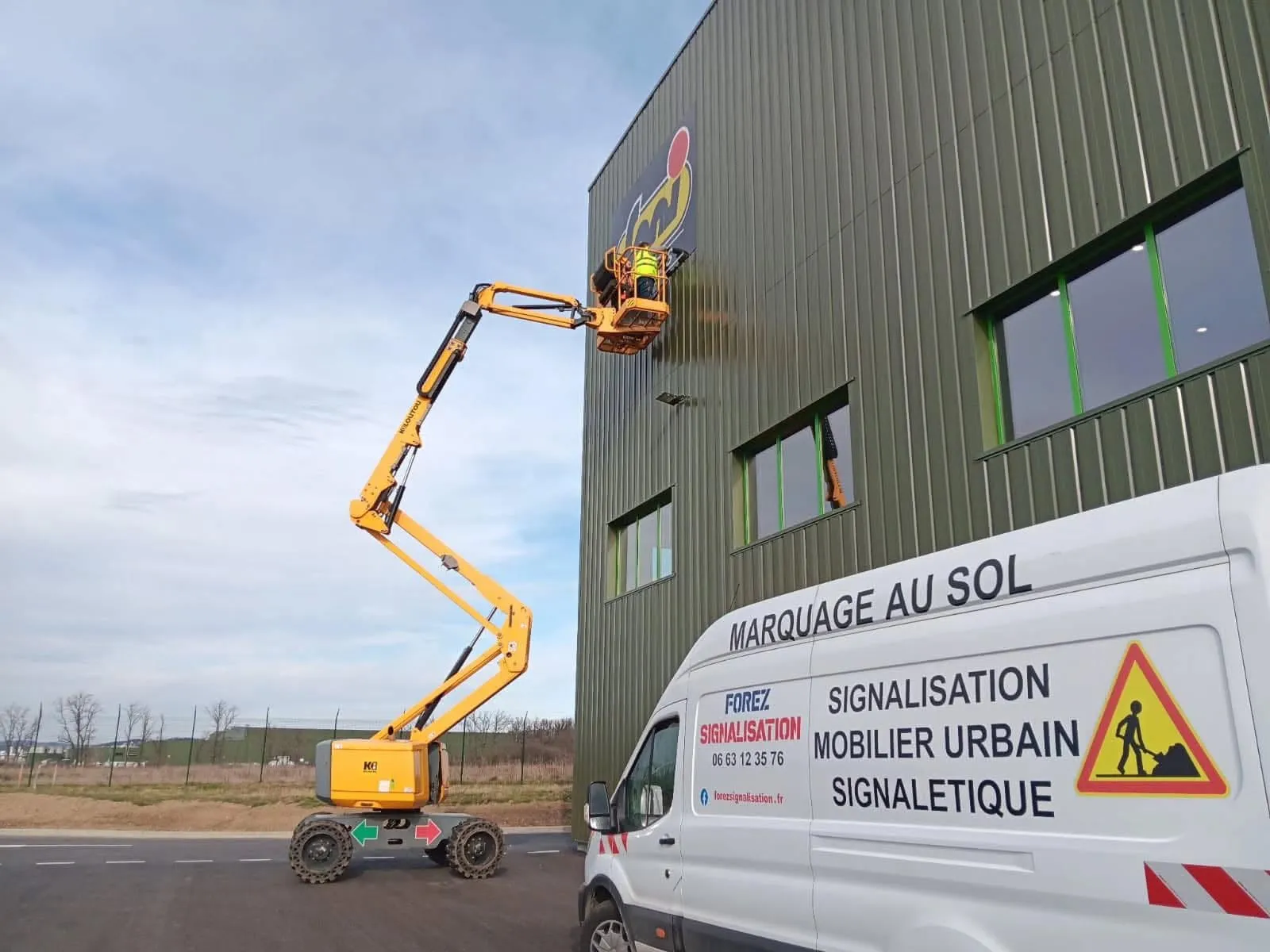 Utilitaire Forez Signalisation au pied d'une façade, nacelle en train de poser une enseigne